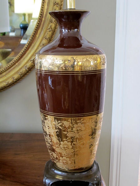 A richly-colored pair of American 1960s chocolate-brown ceramic lamps with fine gilt decoration; each with flaring neck above a tapering body; adorned with gilt perimeter bands depicting delicate meandering floral vines; raised on a metal base with