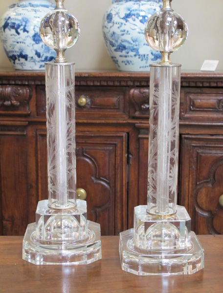 A shimmering pair of American 1950's etched glass columnar-form lamps; each elegant lamp topped with a glass sphere above a cylindrical mid-section with etched floral vine; raised on a square stepped plinth