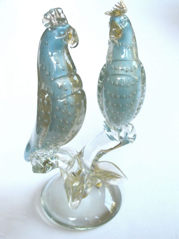 A shimmering Murano mid-century clear and aqua art glass figure of cockatoos; each perched cockatoo with showy crest and curved bill resting on a branchwork base over a circular plinth; all in an encased aqua glass with controlled bubbles and gold