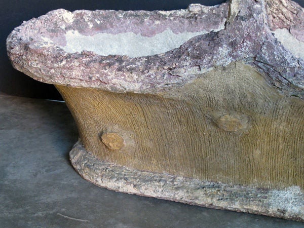 An unusally large French faux bois concrete basket-form jardiniere with arching handle; the rolled bark edge and arching handle above an everted oblong body of simulated grained wood resting on a splayed base