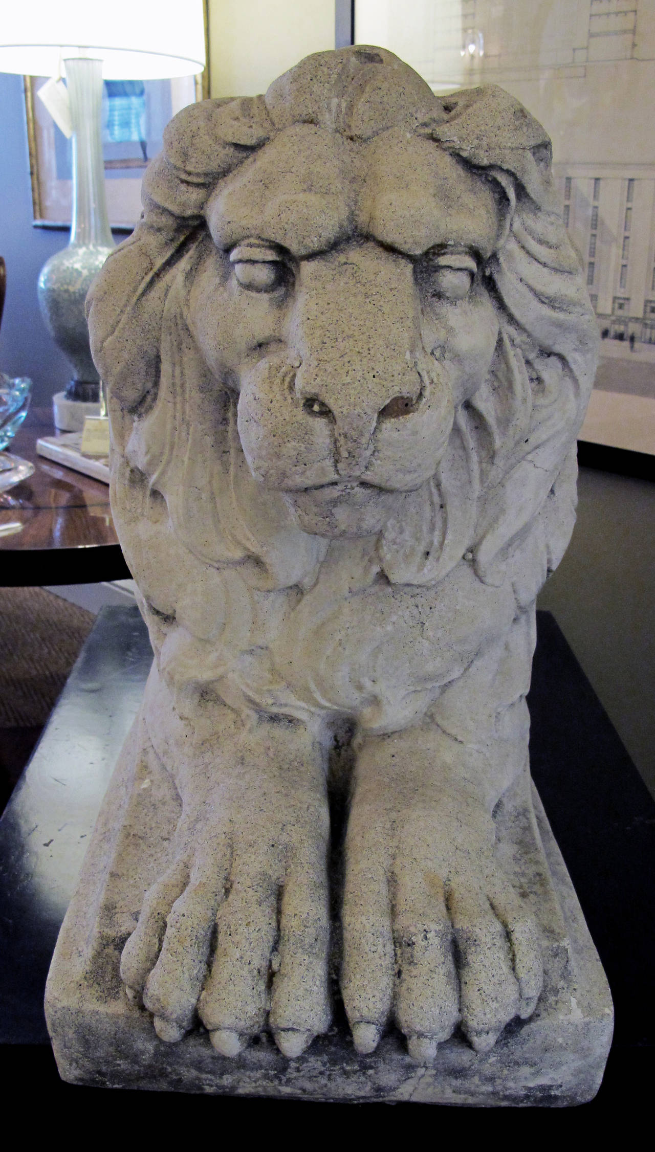 A well-rendered pair of English cast stone garden lions; each recumbent lion with direct gaze surrounded by a thick mane; with well-muscled body and hind quarters