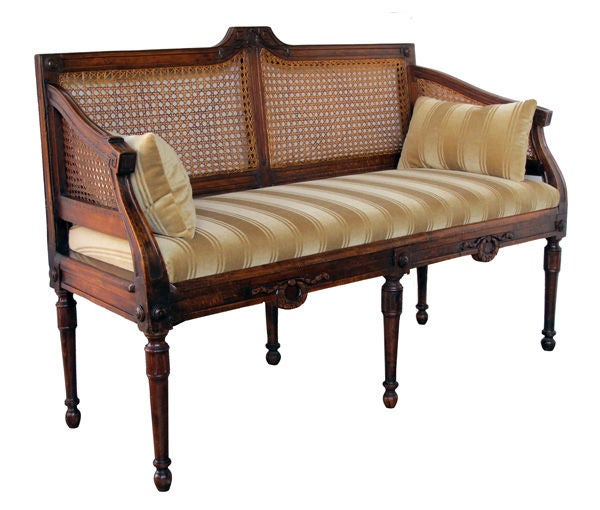A handsome and well-patinated Italian neoclassical walnut settee with caned back and sides; with caned back and sides above an upholstered seat flanked by sloping arms; the apron with carved foliate wreaths all raised on turned supports with a