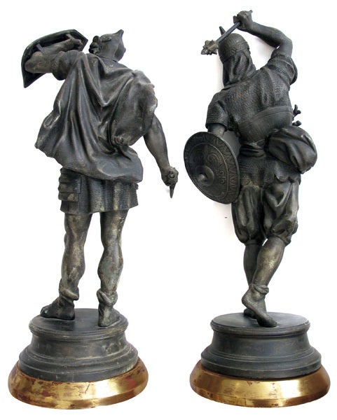 A well-executed pair of English spelter figures of Visigoth warriors; each warrior engaged in battle with shields and weapons dressed mesh armour; raised on splayed bases over giltwood plinths.