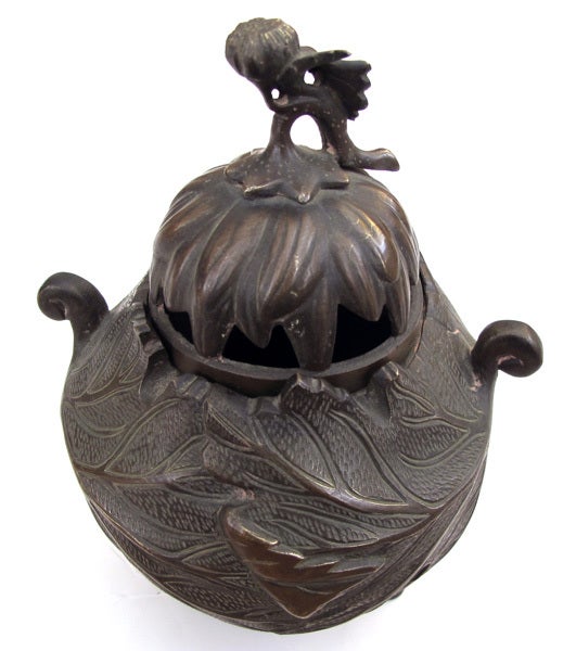 A warmly-patinated Japanese foliate-decorated bronze covered incense burner with chrysanthemum knob; the charming incense burner with domed openwork lid capped by a chrysanthemum stem; resting on a portly body flanked by scrolled handles all adorned