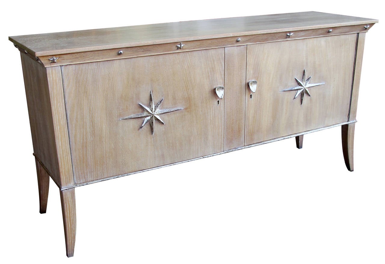 A stylish French Mid-Century two-door cerused oak sideboard with silver-leaf star relief motifs; the solid cabinet with rectangular top above an apron with applied bosses and star motifs over a body fitted with two doors adorned with boldly-scaled