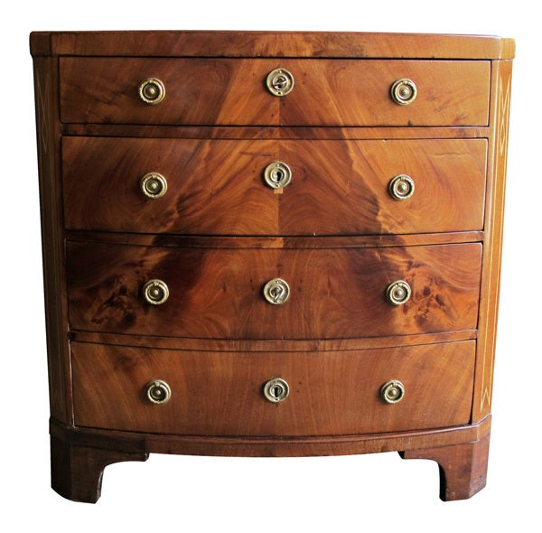 A handsome Danish empire mahogany bow front 4-drawer chest with inlaid canted corners; the bowed top above a conforming body fitted with 4 drawers with flame mahogany veneer flanked by inlaid canted corners; raised on bracket feet