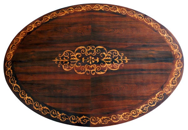 A good Danish late empire brazilian rosewood and parcel-gilt oval tripod center table with scrollwork inlay; the well-figured oval top centering a scrollwork medallion and outer border; raised on a hexagonal support all over a tripartite base with