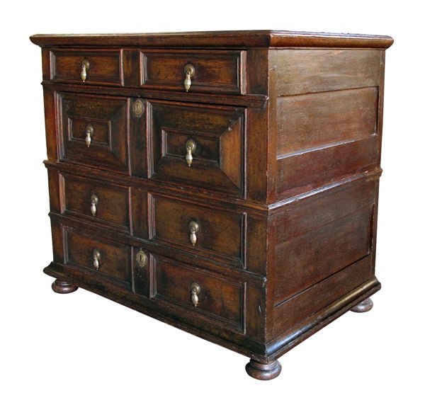 A handsome William and Mary oak 4-drawer chest with bun feet; in two sections, the rectangular top over conforming case fitted with four long drawers with acorn-shaped brass pulls, the second drawer deeper, with raised molded panels