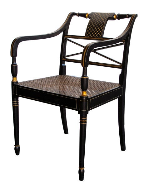 A graceful set of four English regency style black painted and parcel-gilt armchairs with caned seats; one of a later date; each with curvaceous outscrolled chair rails above an x-form splat over a caned seat; flanked by downswept arms with blauster