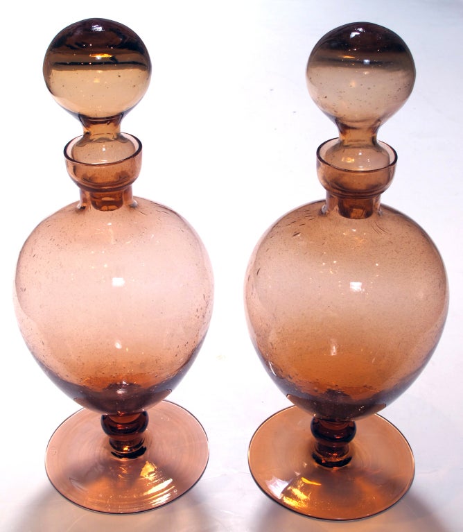 A striking pair of American hand-blown peach-colored apothecary jars; each with hollow stopper resting on an ovoid-shaped body over a circular base with polished pontil; the glass infused with air bubbles