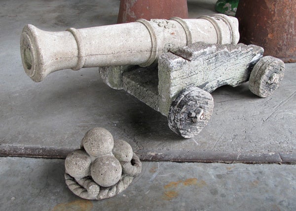 A whimsical French cast stone ship's cannon on a faux bois cart with stacked cannon balls; in 3 pieces; the cylindrical 'iron' cannon resting on a faux bois truck; along with a stack of cannon balls resting on a coiled rope