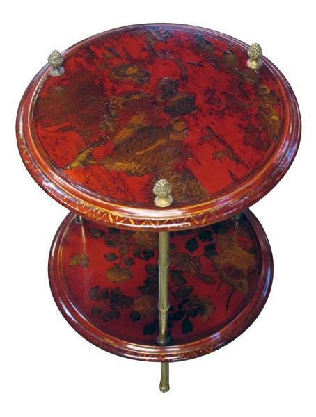An elegant French 1940's 2-tier crimson chinoiserie circular side table with gilt-bronze mounts by Bagues; the circular red lacquered top and lower shelf adorned with tranquil sea and landscape scenes; raised on faux bamboo bronze supports with