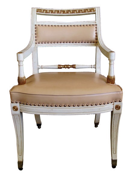 A stylish pair of 1940's Hollywood regency ivory-painted and parcel-gilt Klismos armchairs; each incurved crest with Greek key fret band above a padded back; over an upholstered seat flanked by downswept arms; raised on gracefully splayed legs