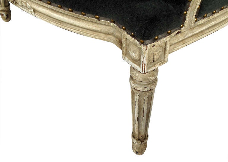 An elegant pair of French Louis XVI style gray-painted and upholstered oval back bergeres; each arching crest surmounted by a carved ribbon above an oval padded back; joining a serpentine seat with loose cushion flanked by padded arms; resting on