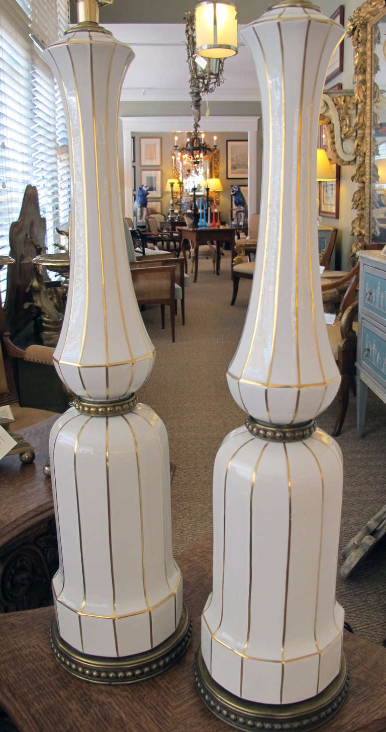 A tall and striking pair of American 1960's ivory porcelain baluster-form lamps with gilt striping; by Lenox; each of faceted ivory porcelain with long neck above a waisted mid-section over a bell-shaped base