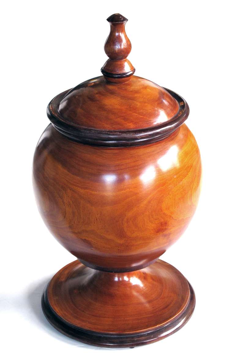 A large-scaled and richly-patinated English treenware lidded pot; the lid with turned finial knob; resting on a spherical body all over a splayed base