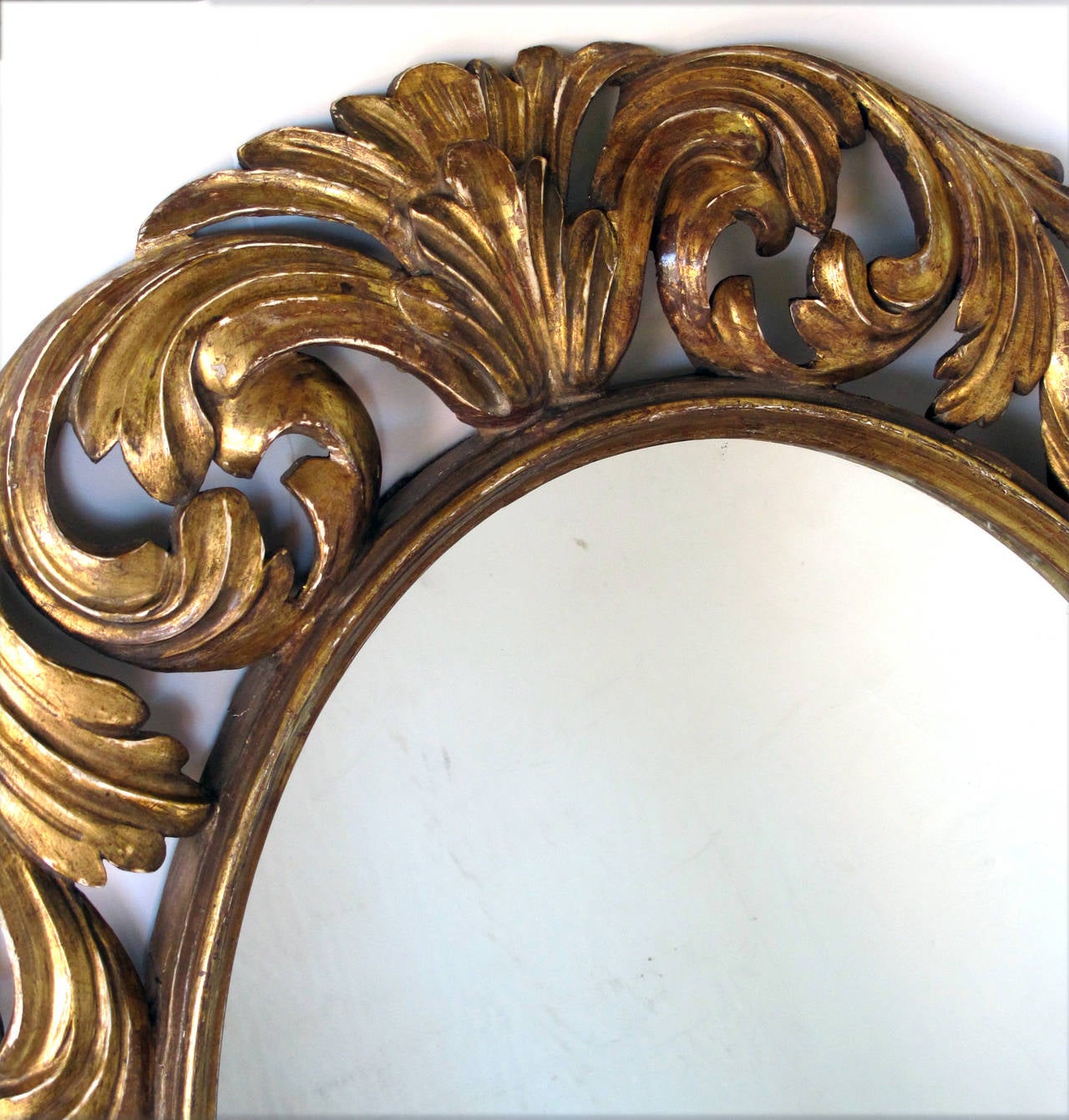 Specchio ovale in legno dorato di stile barocco italiano ben intagliato; la lastra ovale antica all'interno di una sottoveste modanata circondata da un'esuberante decorazione a volute reticolate intagliate