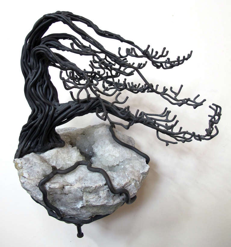 A graceful American 1960's bronze and geode tree sculpture by Belva Ball (1933-2009); composed of shaped and welded bronze rods with outstretched branches, its roots encircling and supporting the large white and gray stone; with metal plate stamped