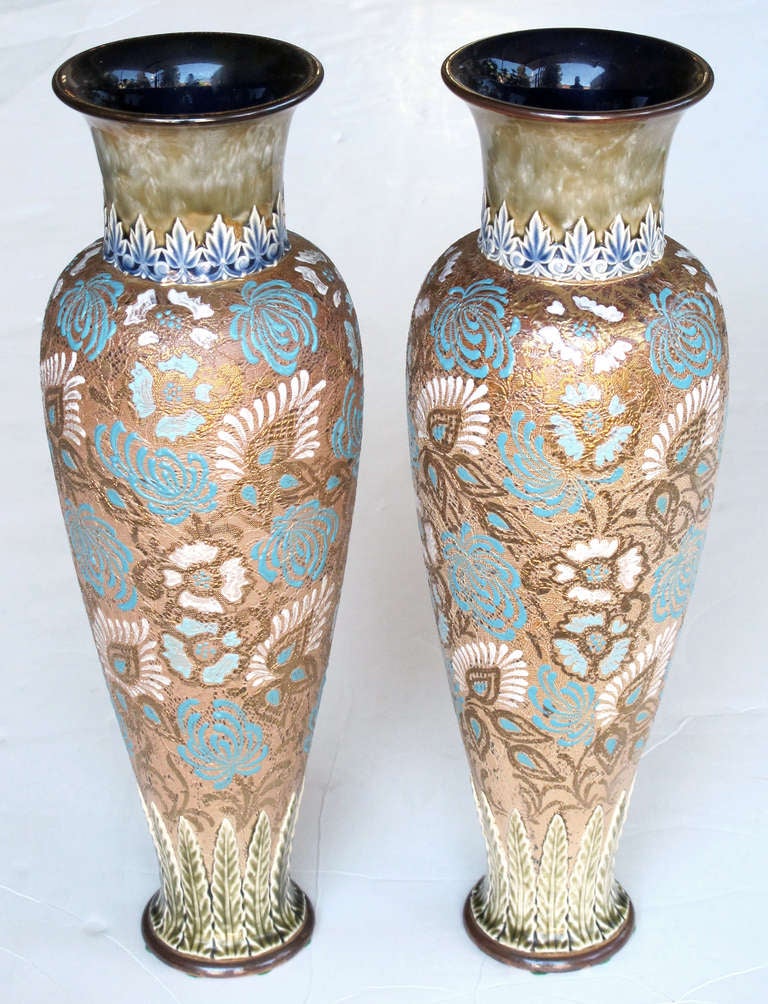 A tall and sleek pair of English Royal Doulton enameled Slater's Patent stoneware vases; each with wide central panel of textured, gilded and hand-painted flower heads all between molded foliate borders; impressed marks on underside