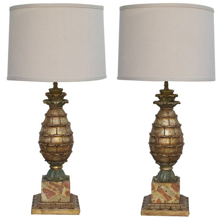 A well-executed pair of Italian painted and parcel-gilt carved wood pineapple-form lamps; each well-carved lamp with flared crown above an imbricated body; all resting on a faux marble plinth