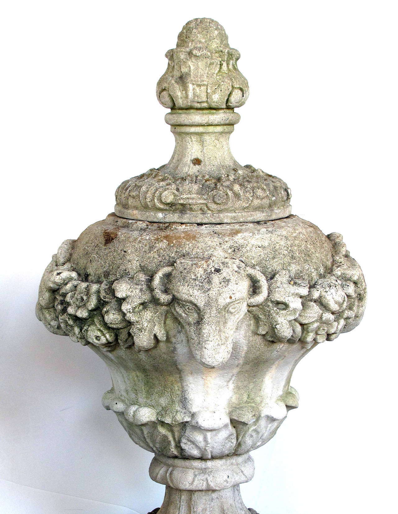A well-delineated pair of English cast stone urn-form finials with swag and ram's head motif; each tall urn with artichoke finial above a urn-form body with lush perimeter swag