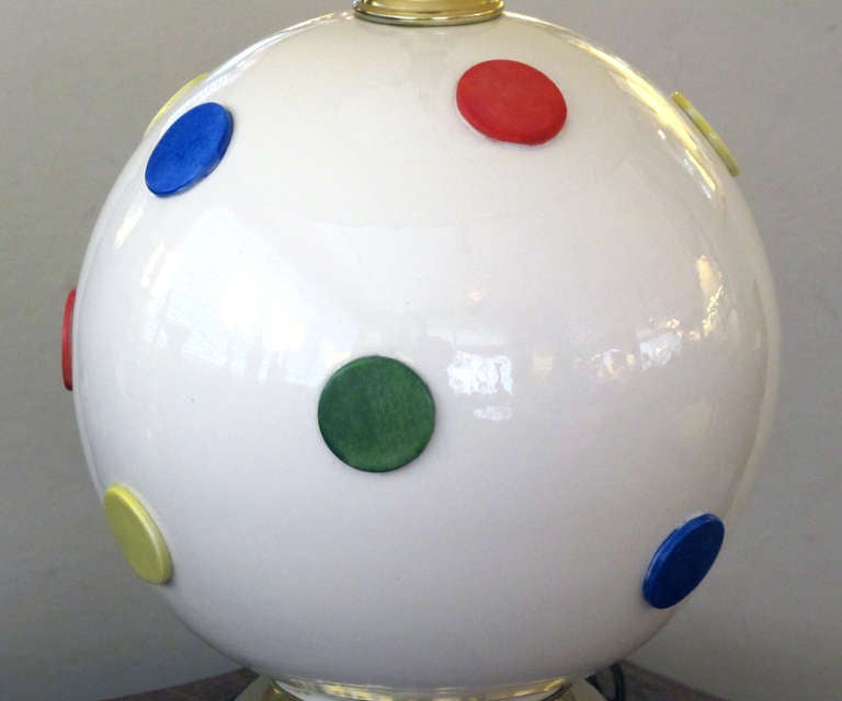 A whimsical pair of American 1960's white ceramic orb-form lamps with colorful polka dots; each white glazed spheroid lamp with applied dots in primary colors; resting on a brass and wooden base