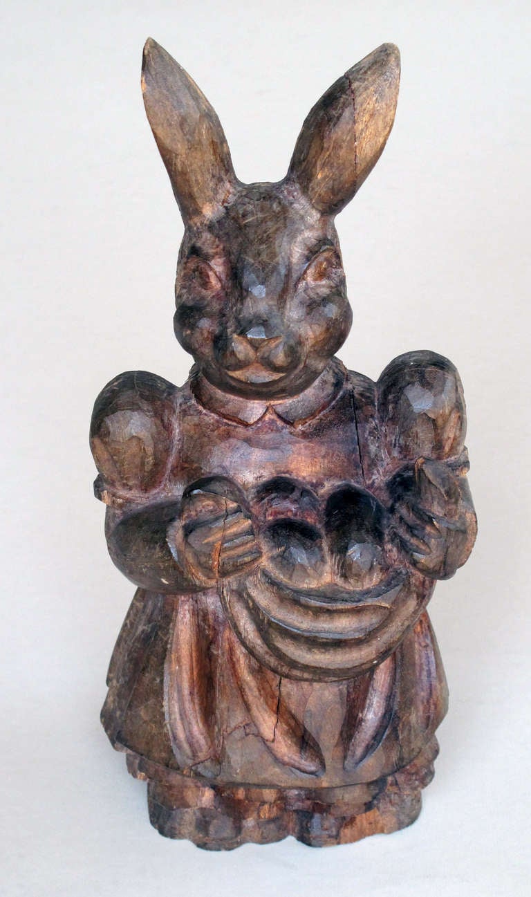 A whimsical American folk art carved wooden rabbit; the delightful carving of a standing rabbit in a simple peasant dress carrying a cloth sling filled with fruit