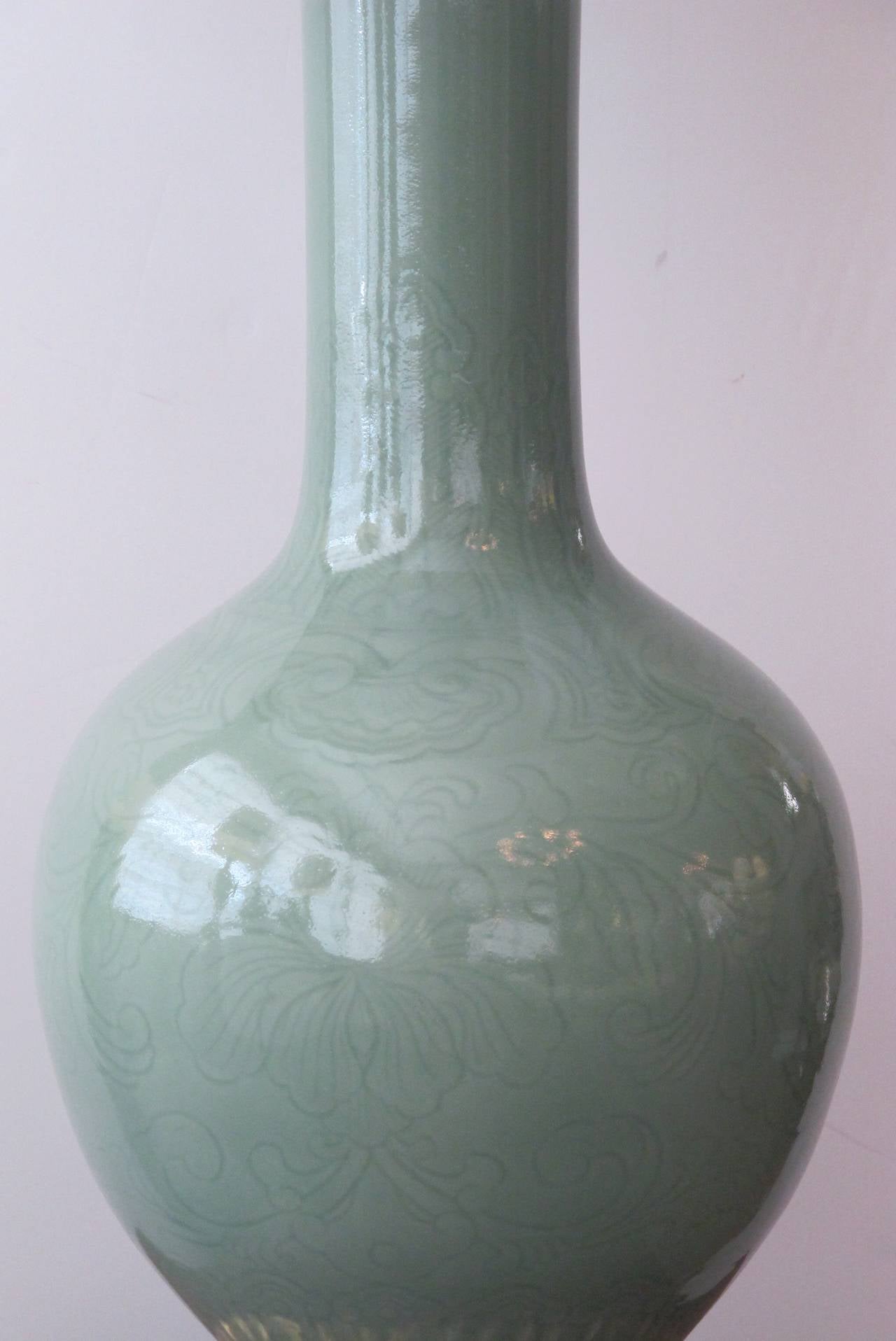 A large-scaled and good pair of Chinese bottle-form celadon lamps on gilt wood bases; each with long neck adorned with incised lappet decoration above a portly body with floral and foliate carving