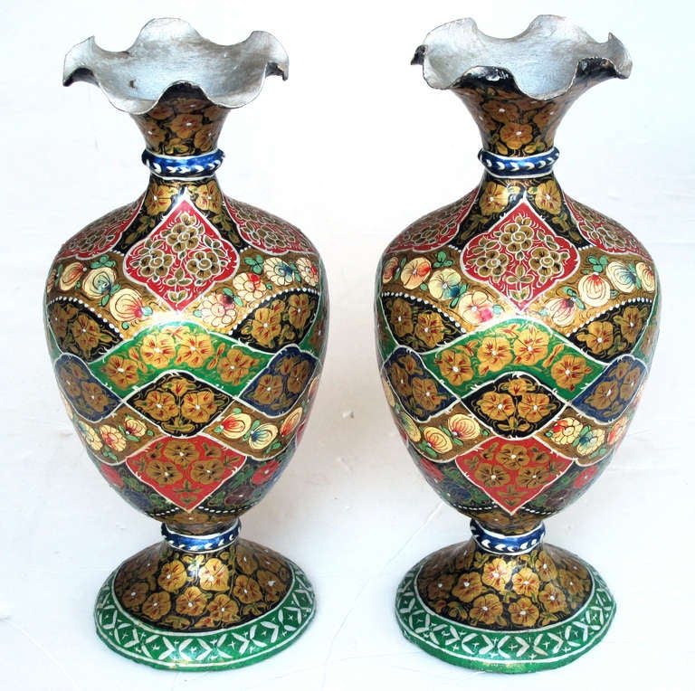 A vibrant and unusual pair of Kashmiri papier mâché polychromed urns; each with ruffled lip above an ovoid body over a splayed base; painted overall with brightly colored floral decoration.