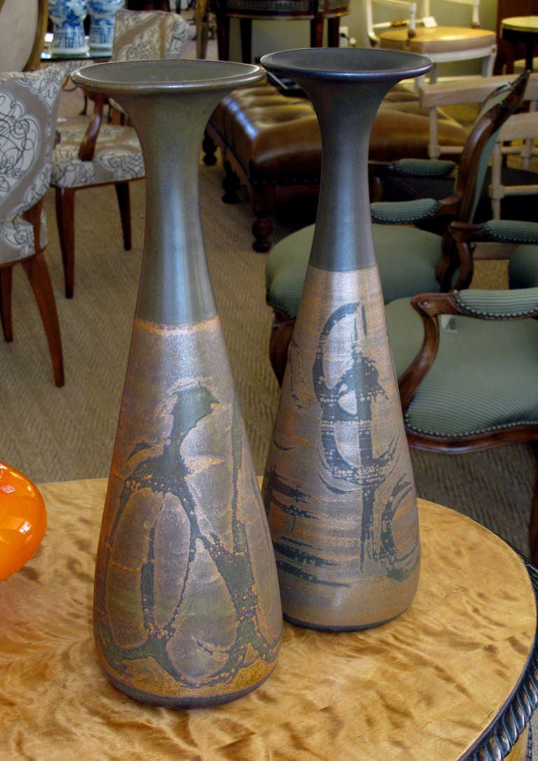 A tall and slender pair of American 1960's brown glazed stoneware bottle-form vases; with foil label 'California Stoneware by Designs West'; each with flaring mouth above a bulbous body; in 2-tone brown glaze with hand decorated abstract designs