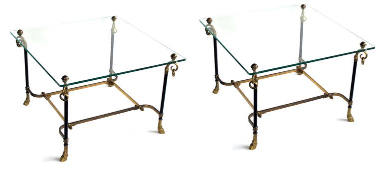 A good pair of French mid-century black tole and gilt-bronze square side tables with glass tops; each square glass top raised on cylindrical supports ending in hoof feet; all joined by a lower stretcher; new glass