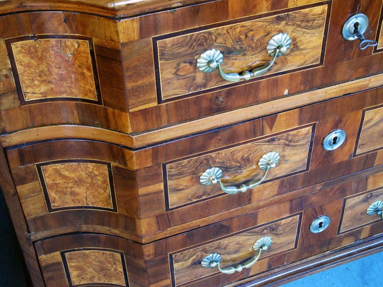 A handsome and richly-patinated German baroque inlaid walnut 3-drawer chest; the shaped top with stepped front above a conforming body fitted with 3 drawers all raised on compressed bun feet