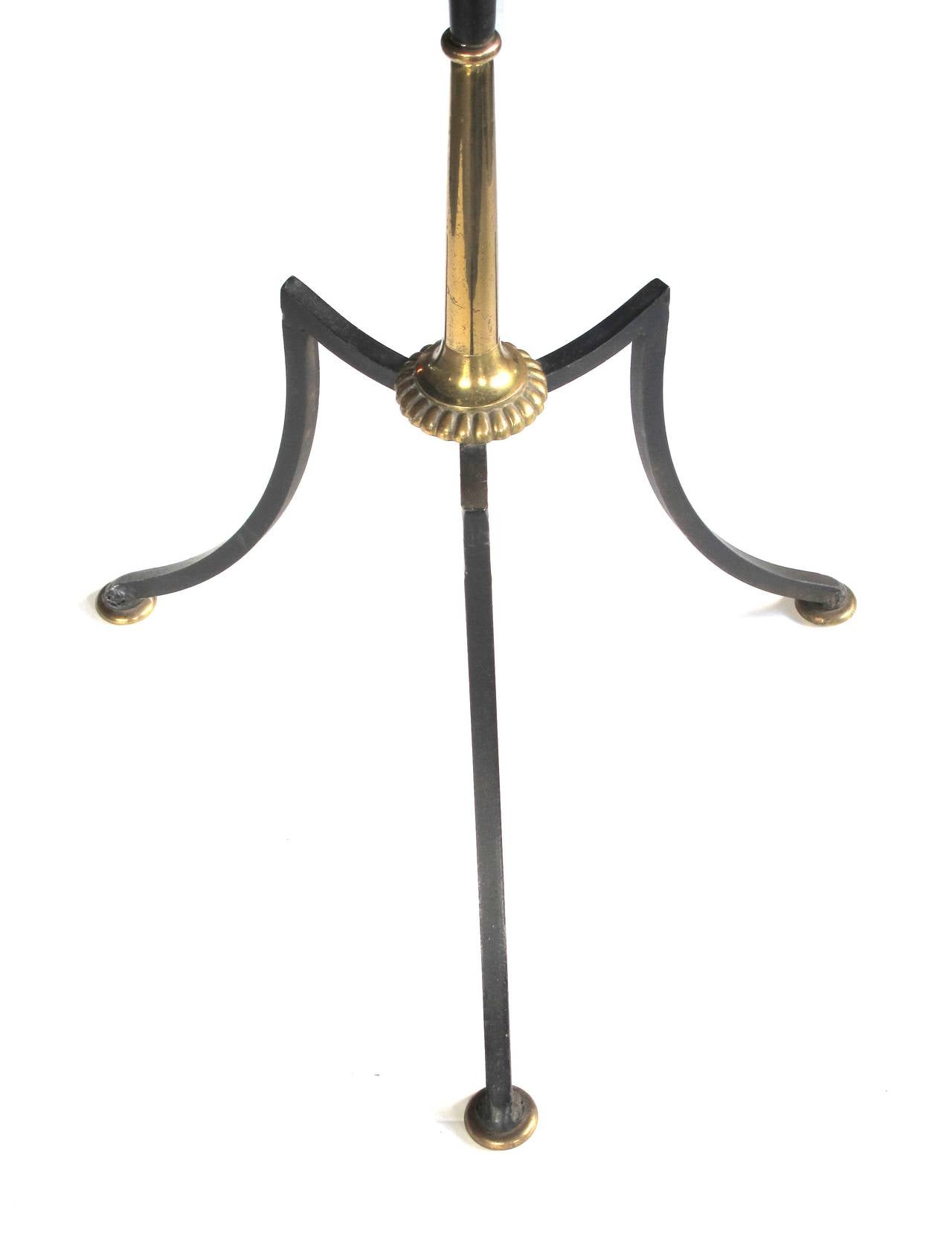 A stylish French 1940's black tole and brass floor lamp; emanating four candlecups from scrolled arms; raised on a tole and brass support over an iron tripod base; custom paper shade
