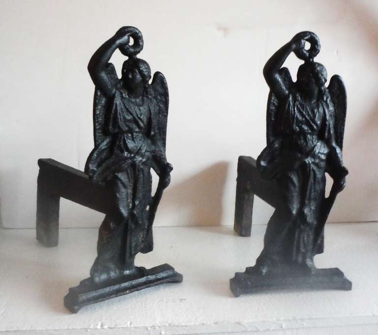 This unusual pair of antique cast iron andirons depicts the first archangel, Michael and dates to the late 19th century.  The pair measures 15 inches high and 13 inches deep front to back.   The andirons show a great patina on the fire logs along