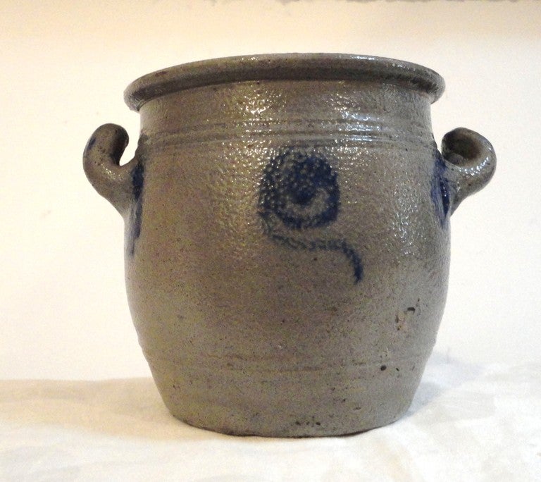 Wonderful 19th century double handled blue decorated salt glaze crock from Pennsylvania. This fine example of Folk Art has decorated handles and front and back with a folky flower. This fun crock is good condition with a minor chip on the lip and