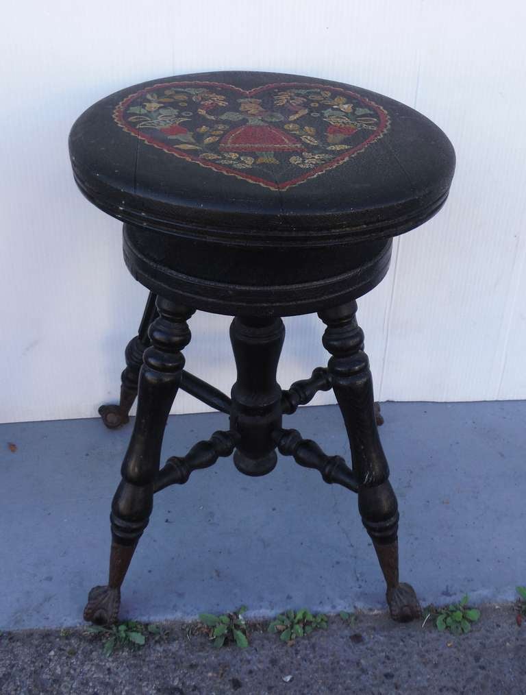 This early Pennsylvania dutch 19thc decorated piano stool has a girl & floral details with in a heart design . The form of the stool is Victorian with cast iron feet with a glass ball & form . The folk art painted heart decoration was done later in