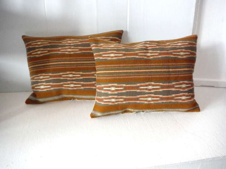 These  interesting geometric wool Navajo Indian weaving bolster pillows contain colors of tan,beige and bittersweet . The condition are very good and have a natural linen backing . Sold as a pair .