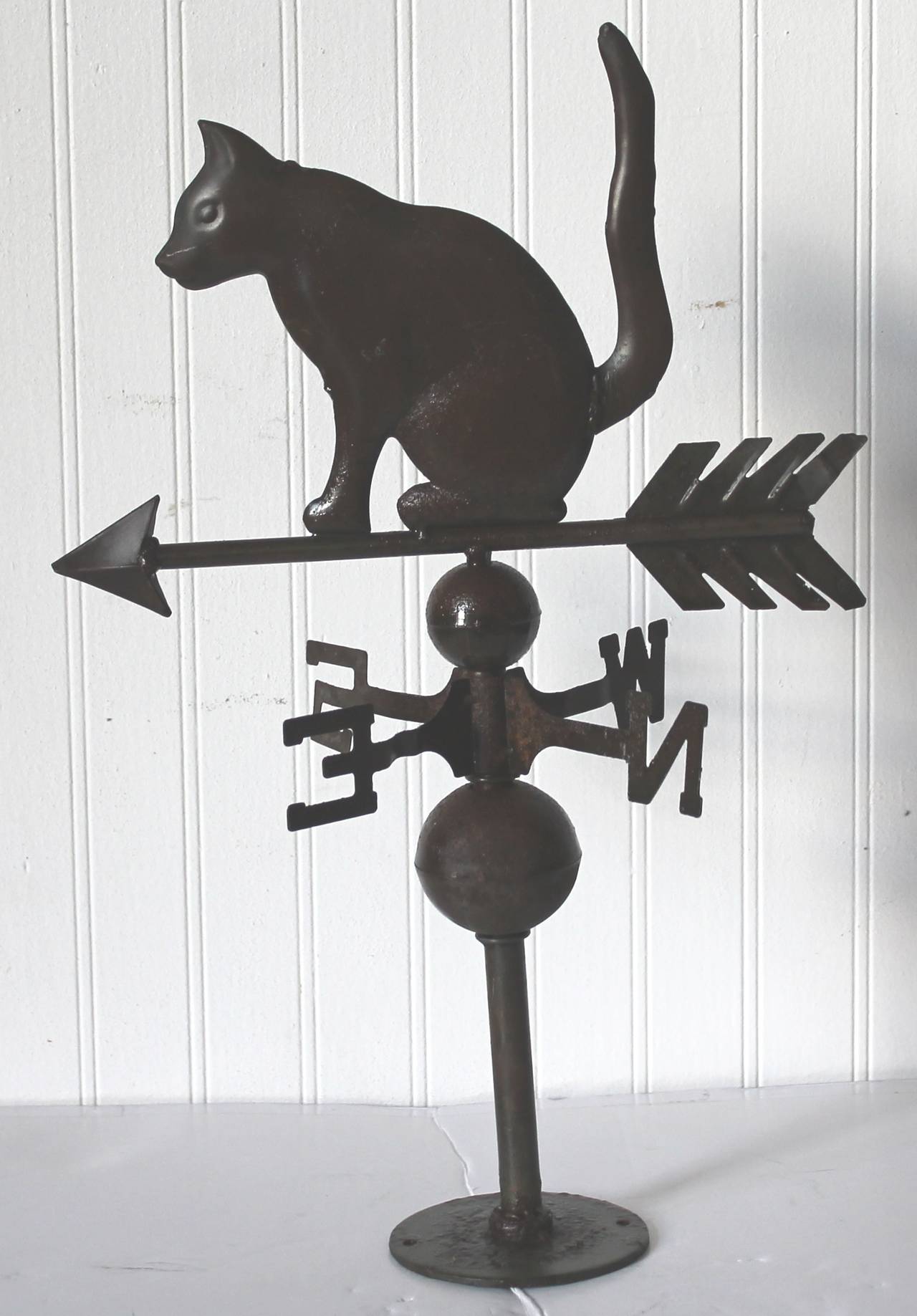 This is such a unusual figurative tin cat weathervane with the original Directional's and base. There is fragments of a olive green original paint remaining on the base. This has the original metal base of which attaches to the roof of the house or