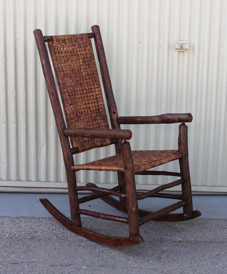 This rustic high back rocker from the Old Hickory Furniture Company of Martinsville is Classic, sturdy and durable. This rocker shows bark with a puritan finish and an open cane weave. The piece is signed Old Hickory Furniture Company of