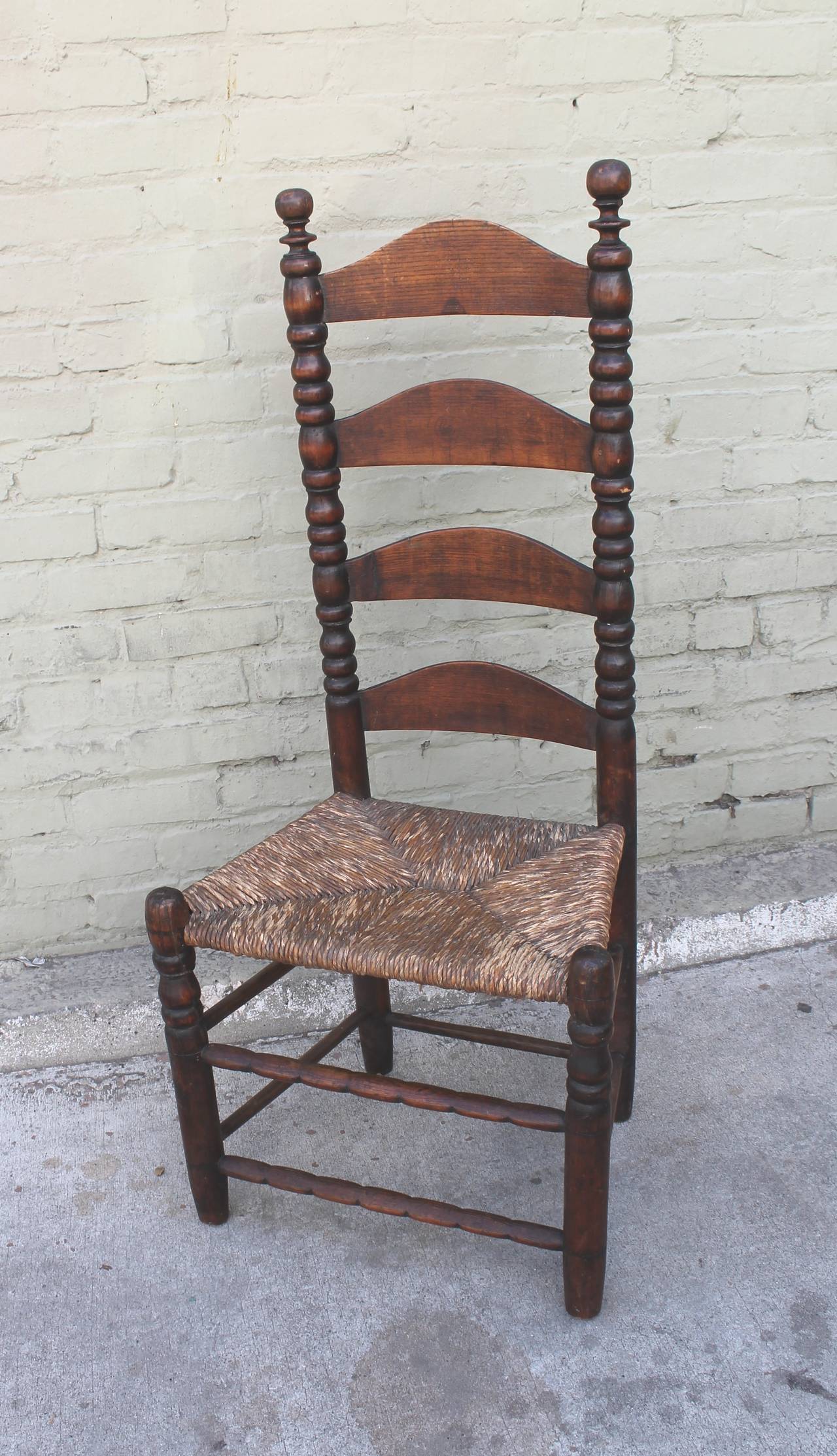 This fine example of early New England ladder back chairs in in very good as found condition. The patina is the very best. The seat is a hand woven rush seat and very sturdy. This chair is from the Gail-Oxford collection. This is a handmade chair.