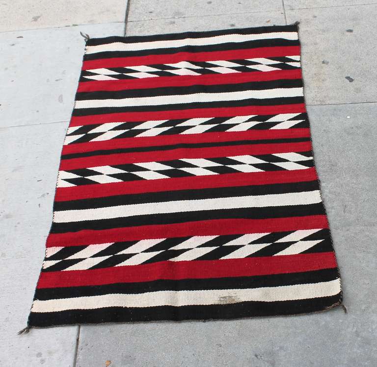 This vibrant Navajo weaving rug is in a bold red, black, cream colors. The condition is good with a minor spot on the lower edge ,cream border . The condition of this rug is very good with the original corner ties .