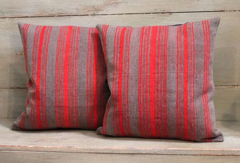 This Classic pair of striped wool pillows is constructed from late 19th century fabric and feature varying sizes of red and brown stripes. The pillows are backed in brown cotton linen and are down and feather filled with bottom zipper closures.