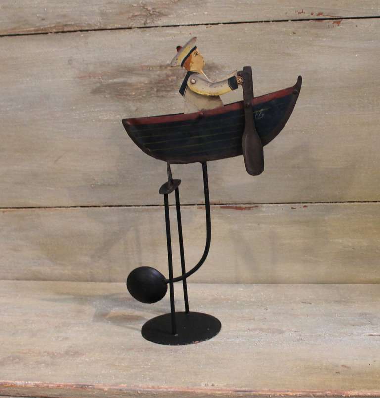 This piece is fully operational and extremely whimsical in design.  The weighted feature when pushed or driven by wind, rocks the sailor's arms to propel the oars creating the illusion of a sailing boat.  Hand nailed and painted in brown, rust,