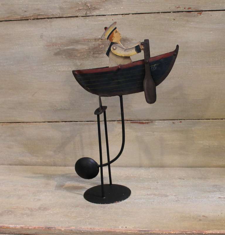 Cette pièce est entièrement opérationnelle et son design est extrêmement fantaisiste.  L'élément lesté:: lorsqu'il est poussé ou entraîné par le vent:: fait basculer les bras du marin pour propulser les rames:: créant ainsi l'illusion d'un bateau à