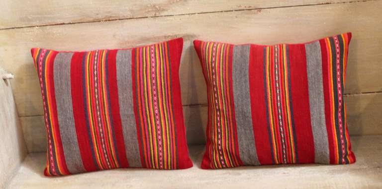 This unusual pair of striped wool pillows is constructed from early 20th century fabric and feature an interesting color palette consisting of red and gray stripes with a multi-toned thick striping of gray, gold, red orange and purple with chain