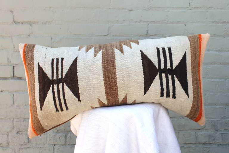 This Navajo woven bolster pillow shows geometric triangular symbols in brown with banded starbursts in tones of gradated dark tan against a cream colored background.  The pillow is backed in camel cotton linen with down and feather fill.
