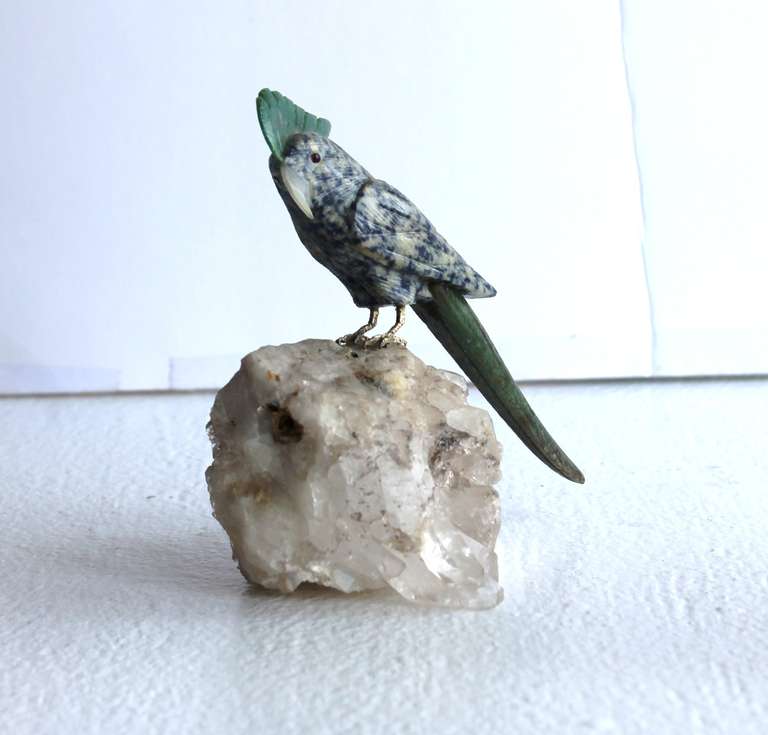 This hand sculpted gemstone cockatoo is perched atop a natural quartz base attached by claws fashioned of sterling silver and gilt.  With garnet eyes, the body is formed of blue and white sodalite with crest, tail feathers and beak carved from