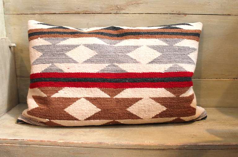 This Navajo woven bolster pillow in a crystal pattern shows horizontal stripes and geometric triangulated patterns. The triangles are shown in gray and dark tan with a cream background. The stripes are represented in dark tan, black and wine. The