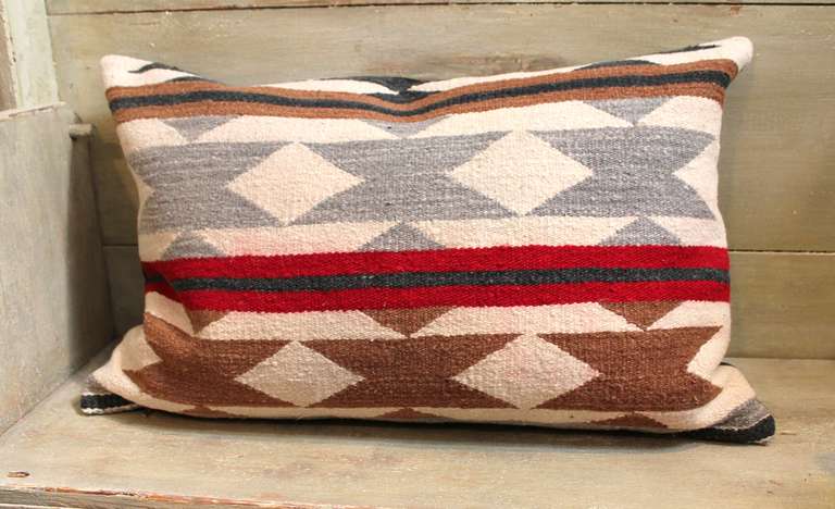 This striking Crystal Navajo Woven Bolster Pillow shows horizontal stripes and geometric triangulated patterns.  The stripes are represented in dark tan, black and wine - the triangles are in gray and dark tan, landscaped in cream.  The pillow is