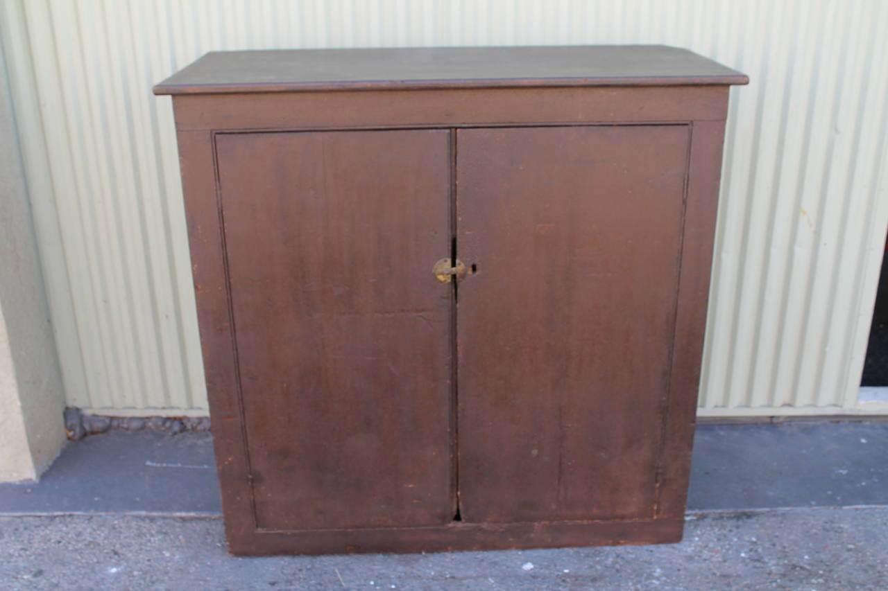 This fantastic and rustic two-door cabinet was found in New England. It has a grungy brown surface with a wonderful chrome yellow or mustard interior. The undisturbed surface is great and so is the construction. It is early square nails with all